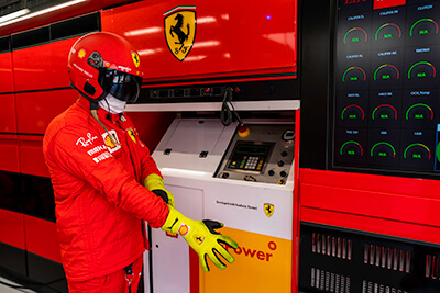 V-Power team wearing driver gear with helmet looking at dashboard analysis and metrics for racing performance